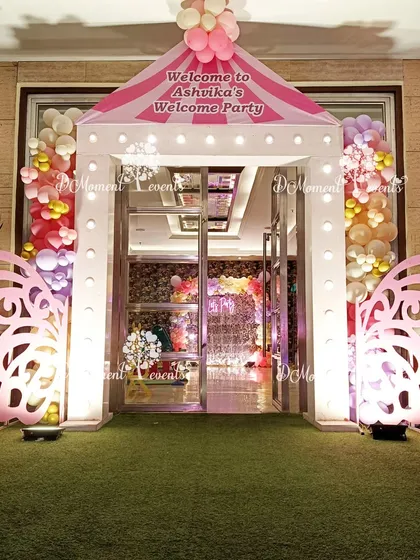 A beautiful entrance for Ashvika's welcome party, featuring a house-shaped arch with illuminated butterfly wings. The pink and white color scheme creates a sweet and inviting atmosphere for guests.