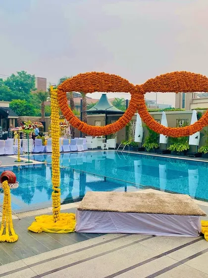A fun and quirky poolside Haldi setup featuring a large pair of sunglasses made entirely of marigolds. This unique prop serves as a perfect photo opportunity for guests.