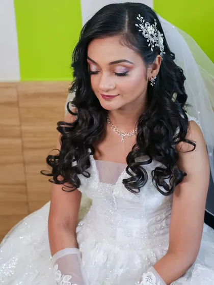 The finished look. The bride looks serene and beautiful with her soft curls, shimmery eye makeup, and a classic white gown.