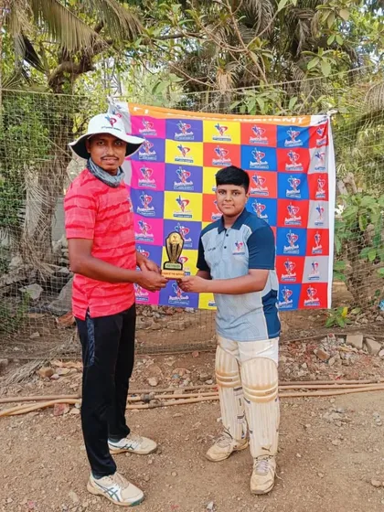 A U-14 player in full batting pads receives his Man of the Match trophy right after coming off the field.