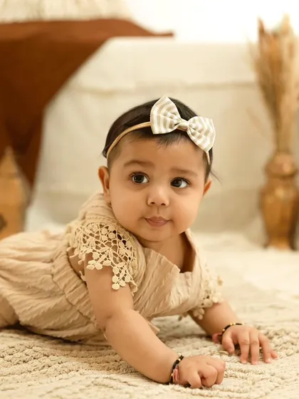 A sweet baby girl in a beige romper during her sitter session. The neutral tones and soft textures create a warm and gentle portrait.