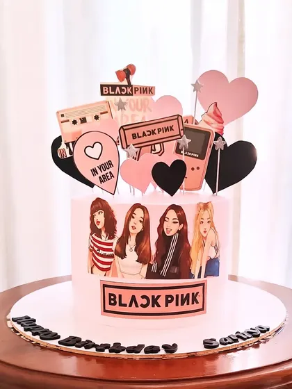 A Blackpink-themed cake for a K-Pop fan. The pink cake is decorated with edible images of the group and fun, retro elements like a cassette tape and a Gameboy.