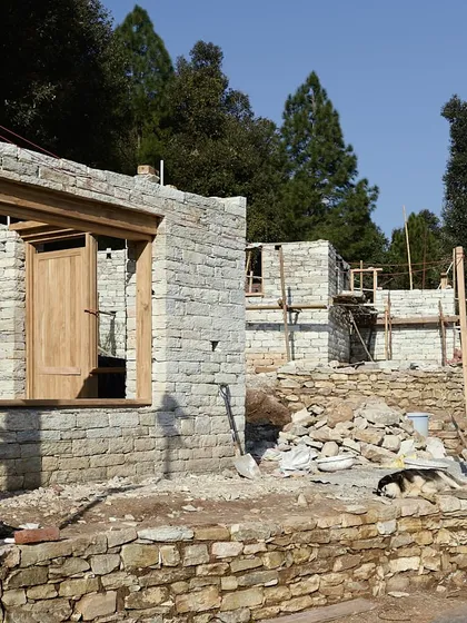 A dog rests in the sun next to a stone wall under construction in Uttarakhand. This image captures a quiet moment on site, where the slow, patient process of building by hand unfolds day by day.