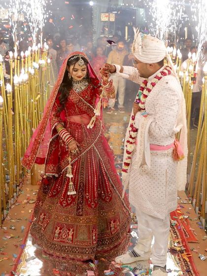 A magical entry. The bride and groom walk in amidst sparklers, and her red lehenga and flawless makeup shine through, creating a truly cinematic moment.