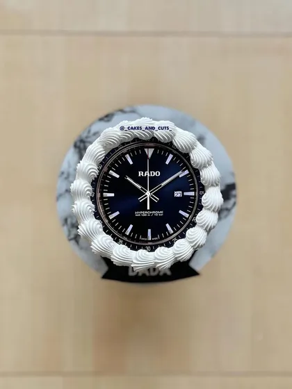 A top-down view of the RADO watch cake, showing the detailed watch face and buttercream piping.