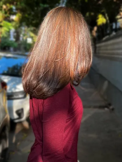 A side profile showing the sleek finish and subtle color of her hair in the sunlight. This is a great example of a natural-looking hair color enhancement.
