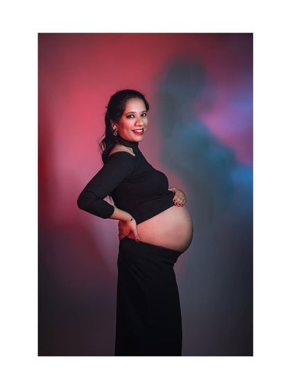 A chic maternity portrait with creative colored lighting. The mother-to-be glances at the camera with a smile, showcasing a bold and modern style.