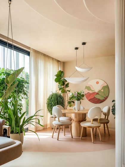 The dining area is defined by a change in the microcement flooring color. Surrounded by plants and lit by a minimal chandelier, it feels like a serene, inviting space for meals while staying connected to the living area.