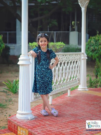 Posing like a little star. This confident portrait was taken outdoors, showcasing a stylish blue dress against the natural backdrop of a park.