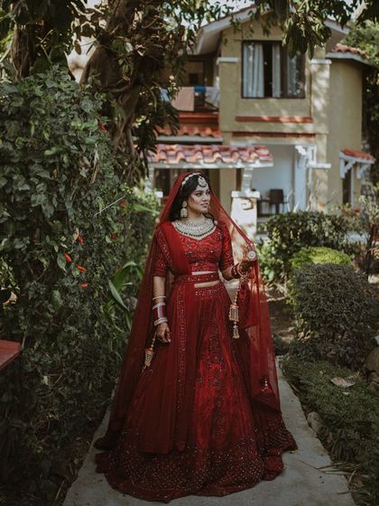A full-length portrait of the bride in her stunning red lehenga, walking through a lush garden. A moment of grace and anticipation.