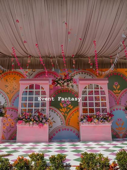 A full view of the vibrant and whimsical Mehandi stage. I used a custom-painted backdrop with colorful, playful patterns and faux window frames to create a unique, carnival-like atmosphere.