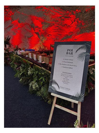The menu for our Goan "Poi Bar" is displayed on an easel against a stunning, dramatically lit rock formation. This shows how we integrate our setups into the natural beauty of the event location.