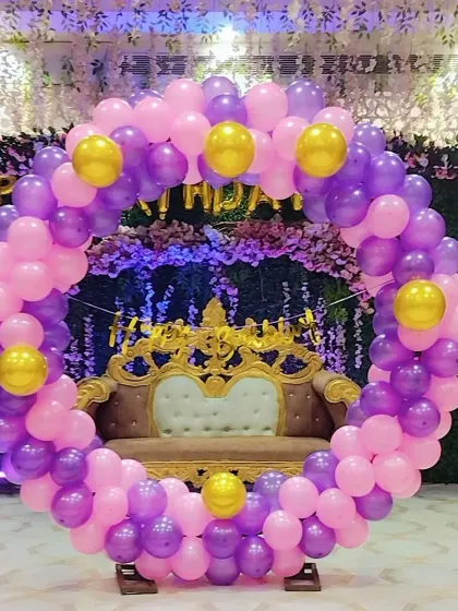 A royal-looking birthday setup with a purple and pink circular balloon arch framing a small sofa.