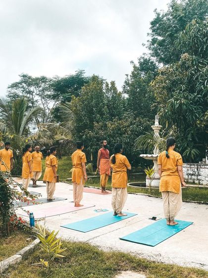 From our yoga shala, you can see students practicing Ardha Uttanasana (Half Standing Forward Bend) in the garden. The serene backdrop of mango trees and open sky makes every practice a communion with nature.