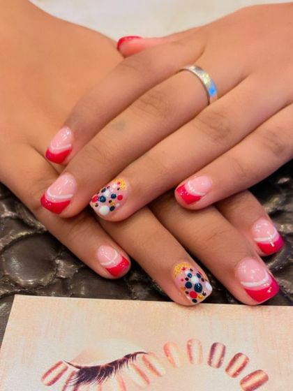 A fun and playful design on short, natural nails. The look features a red French tip with accent nails that have a dotted, multi-color pattern.