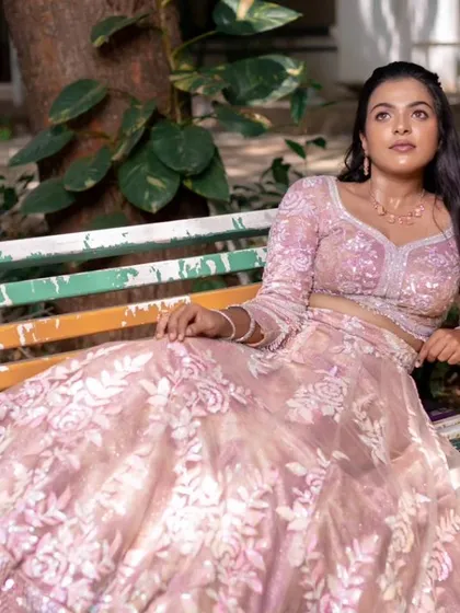A model sitting on a colorful bench, showcasing a modern reception look with a beautiful pink lehenga and soft, natural makeup.