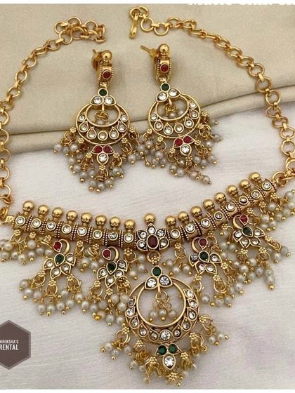 A close-up of a beautiful rental necklace and earring set, featuring intricate work with multi-colored stones and pearl drops.