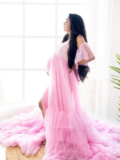 A graceful silhouette of a mom-to-be in a pink gown, standing against a bright window, highlighting her beautiful pregnancy figure.