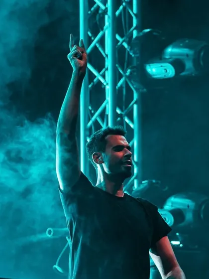 Afrojack raises a hand to the sky, surrounded by a cool blue haze.