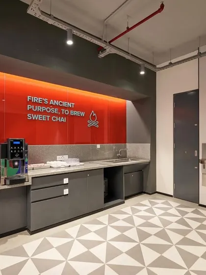A modern pantry area with sleek grey cabinetry and a red glass backsplash with the quote "Fire's ancient purpose, to brew sweet chai".