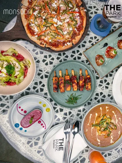 A beautiful overhead shot of a meal at Monsoon, featuring wood-fired pizza, paneer tikka, fresh salads, and rich curries.