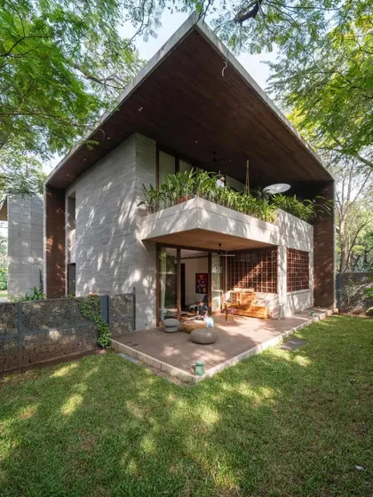 The exterior of the Maheshwari house is a beautiful example of tropical modernism, with its board-formed concrete walls, deep wooden roof, and lush garden setting.