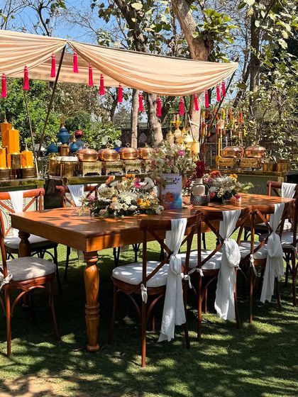 Another view of the elegant long table setup for the Holi party. The canopy with red tassels provides shade and adds a touch of traditional flair to the modern rustic setting.