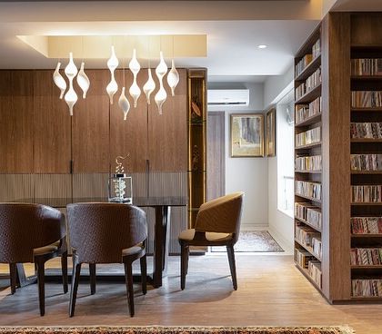 This dining area, part of the 'Library of Music' residence, is surrounded by floor-to-ceiling bookshelves. A modern, sculptural light fixture hangs above the dining table, creating an intimate and sophisticated space for meals and conversations.