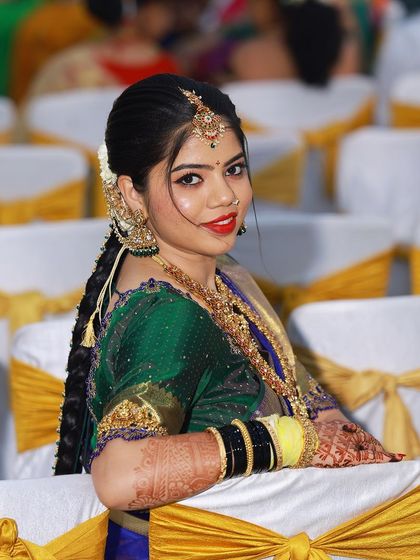 A beautiful bride in a royal blue and green Kanjeevaram saree. The makeup features a bold red lip and smoky eyes.