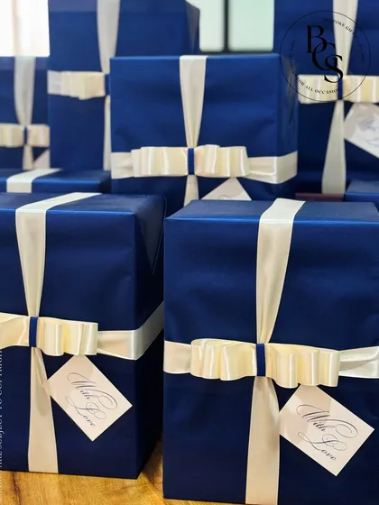 A stack of beautifully wrapped gifts in a deep royal blue. The classic wrapping is elevated by a contrasting cream-colored satin ribbon and a personalized "With Love" tag, ideal for a formal event or corporate gesture.