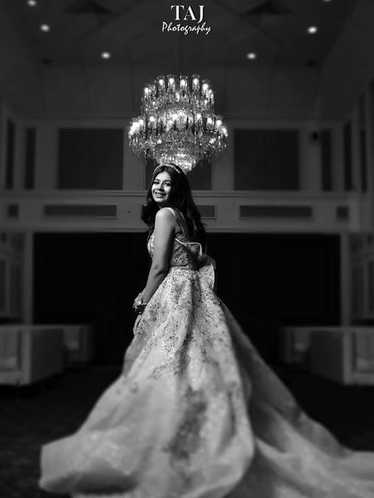 A glamorous black and white portrait of the bride in her reception gown. The grand chandelier and her joyful expression create a classic, celebratory image.