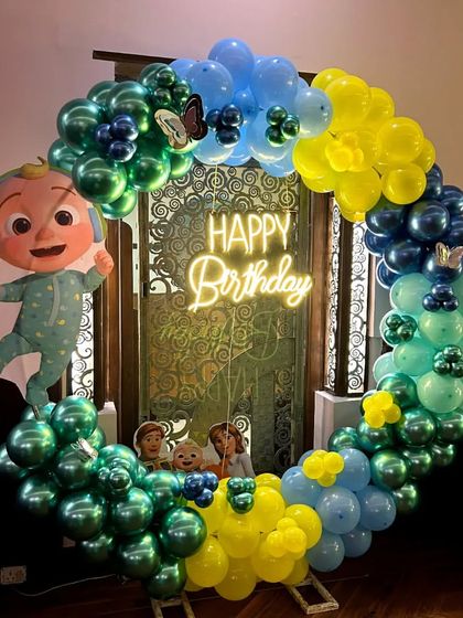 A Cocomelon-themed birthday ring in green, blue, and yellow, with a character cutout and a "Happy Birthday" neon sign.