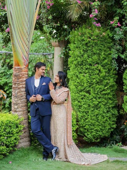 A stylish portrait of a couple in a lush garden, him in a sharp blue suit and her in a beautiful embellished lehenga.