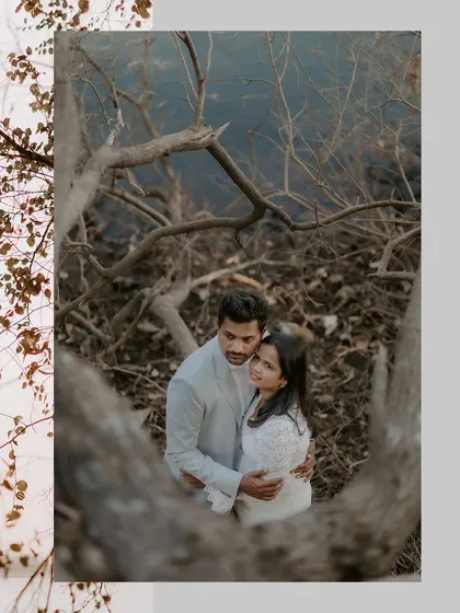 An artistic shot looking down on a couple embraced amongst the tangled branches of trees by a lake, creating a unique and intimate natural frame.