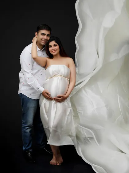The goddess is here. This studio portrait captures the couple in a loving embrace, with a flowing white fabric adding a touch of ethereal beauty.
