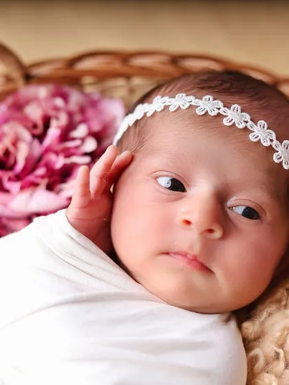 A close-up portrait of a newborn in a white swaddle, looking thoughtfully to the side. This captures a quiet, contemplative moment.