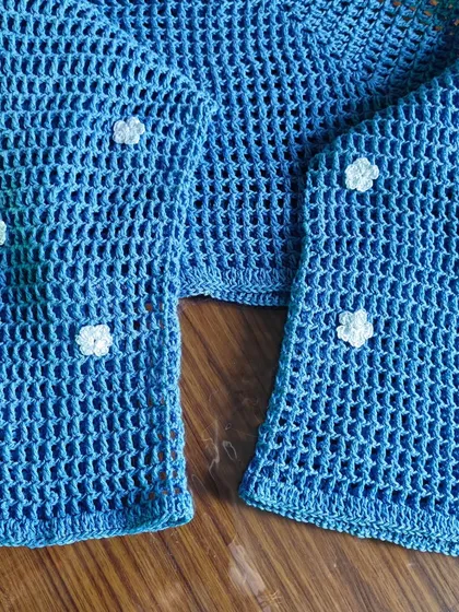 A close-up of the sleeve detail on the blue mesh shrug, showing the small, hand-stitched white flowers that give it a unique, delicate look.