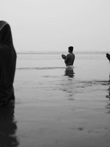 Devotees stand in the river at dawn, offering prayers to the sun god in a stark, minimalist black and white composition that emphasizes their faith.