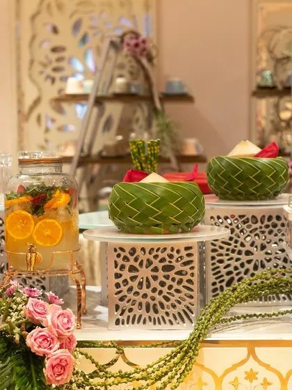 An elegant beverage station with a large glass dispenser of citrus-infused water and woven leaf bowls. The setup is both beautiful and functional, offering guests a refreshing drink option.