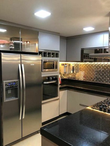 A compact and luxurious kitchen design. This space features reflective high-gloss cabinets, a patterned tile backsplash, and integrated stainless steel appliances, maximizing both style and efficiency in a smaller footprint.