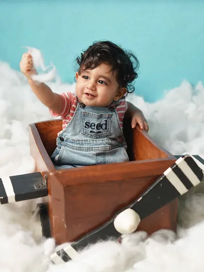 Another little pilot in the clouds, this time playing with the soft cotton. The denim overalls and striped shirt add a classic, boyish charm.
