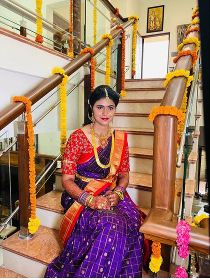 A full view of the client seated on the stairs, giving a great perspective on the complete traditional attire and makeup for her pellikuthuru.