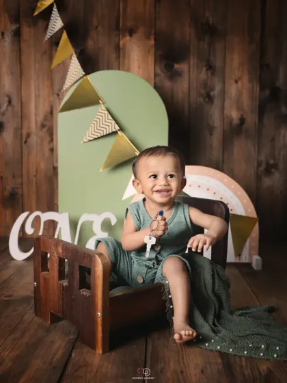 A happy one-year-old boy celebrating his first birthday. This rustic-themed studio setup features a wooden backdrop, a miniature bed, and 'ONE' sign props.