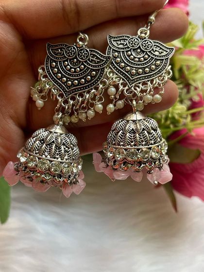 A close-up of the silver-oxidised jhumkas with uncut pink beads and stone work on the dome, showing the intricate detailing.