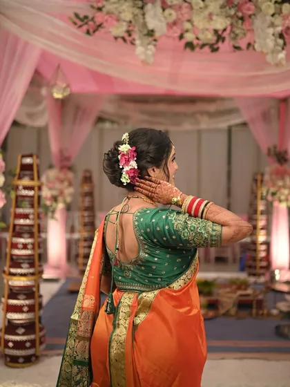 A view of the bride's back, showcasing her elegant bun hairstyle adorned with flowers and the beautiful design of her blouse.