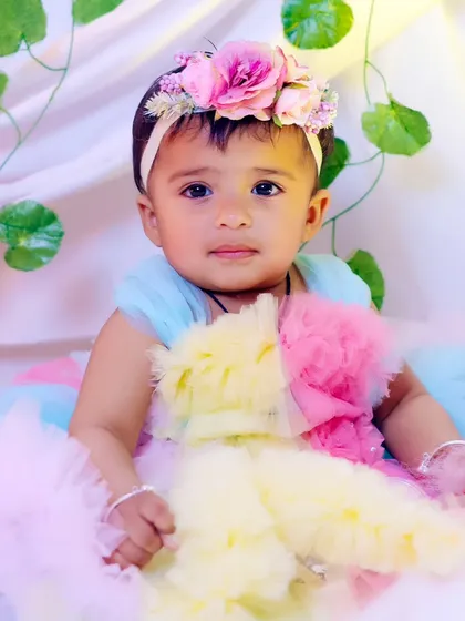 A close-up portrait of the baby girl in her floral headband and pastel dress.