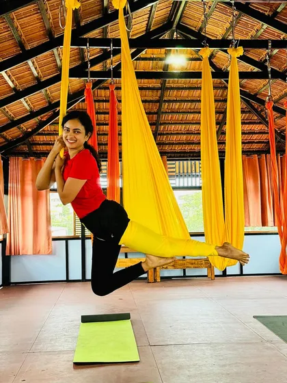 A student smiles as she practices a suspended pose in the yellow hammock, enjoying the process of learning and growing.
