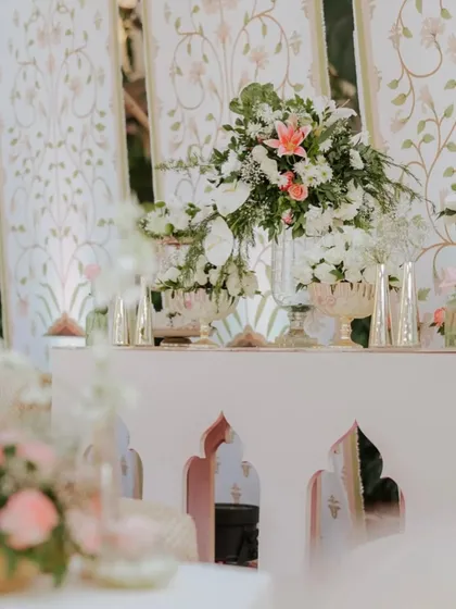 A detail shot of the decor for the 'Ivory Clad Promises' wedding, featuring a console table with fresh white and pink floral arrangements set against intricately carved panels.
