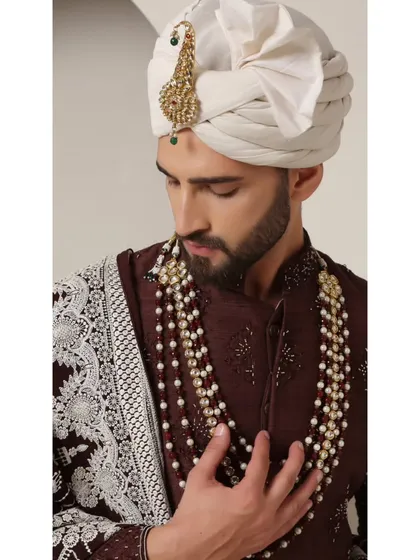 A closer look at the Coco Royal sherwani, highlighting the intricate booti motifs and the contrast of the ivory pearls against the deep brown fabric.