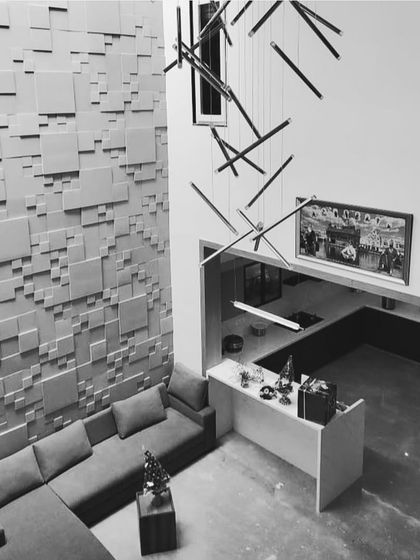 The 'Recursion' concrete wall panels installed in a double-height living room. The varying depths of the squares create a dynamic, geometric tapestry that serves as a monumental art piece in itself.